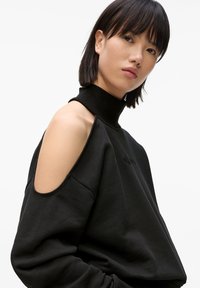 Fekete kapucnis pulóver magas nyakkal és hideg vállas kialakítással. Puha tapintás, lazán illeszkedő, a fronton diszkrét logóval.