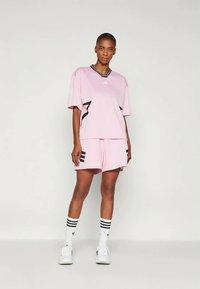 Rosa idrottsset med en löst sittande t-shirt med svart krage och detaljer, ihop med matchande shorts och randiga knästrumpor.