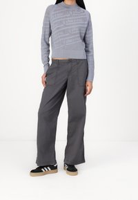 Pull en tricot bleu clair avec un motif, associé à un pantalon gris ample et des baskets noires avec des rayures blanches et des semelles beige.