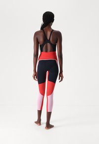 Black tank top with racerback design; form-fitting leggings featuring red, navy, and pink color blocks and a high waistband.