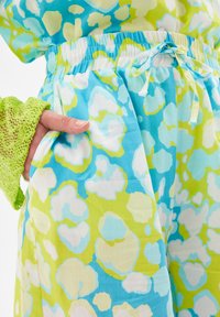 Luźne, lekkie spodnie z intensywnym abstrakcyjnym wzorem w odcieniach niebieskiego, zielonego i białego. Elastyczny pas z troczkiem oraz kieszeń boczna.