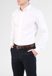 Witte lange mouwen shirt met een button-down kraag, gecombineerd met marineblauwe broek en een leren riem in bruin. Slim fit, gladde textuur, minimalistisch ontwerp.