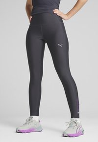 Musta stretch-legginset korkealla vyötäröllä, joissa on hopeinen Puma-logo ja violetit yksityiskohdat alareidessä. Pehmeä, sileä kangas, jossa on ompelut yksityiskohtia.