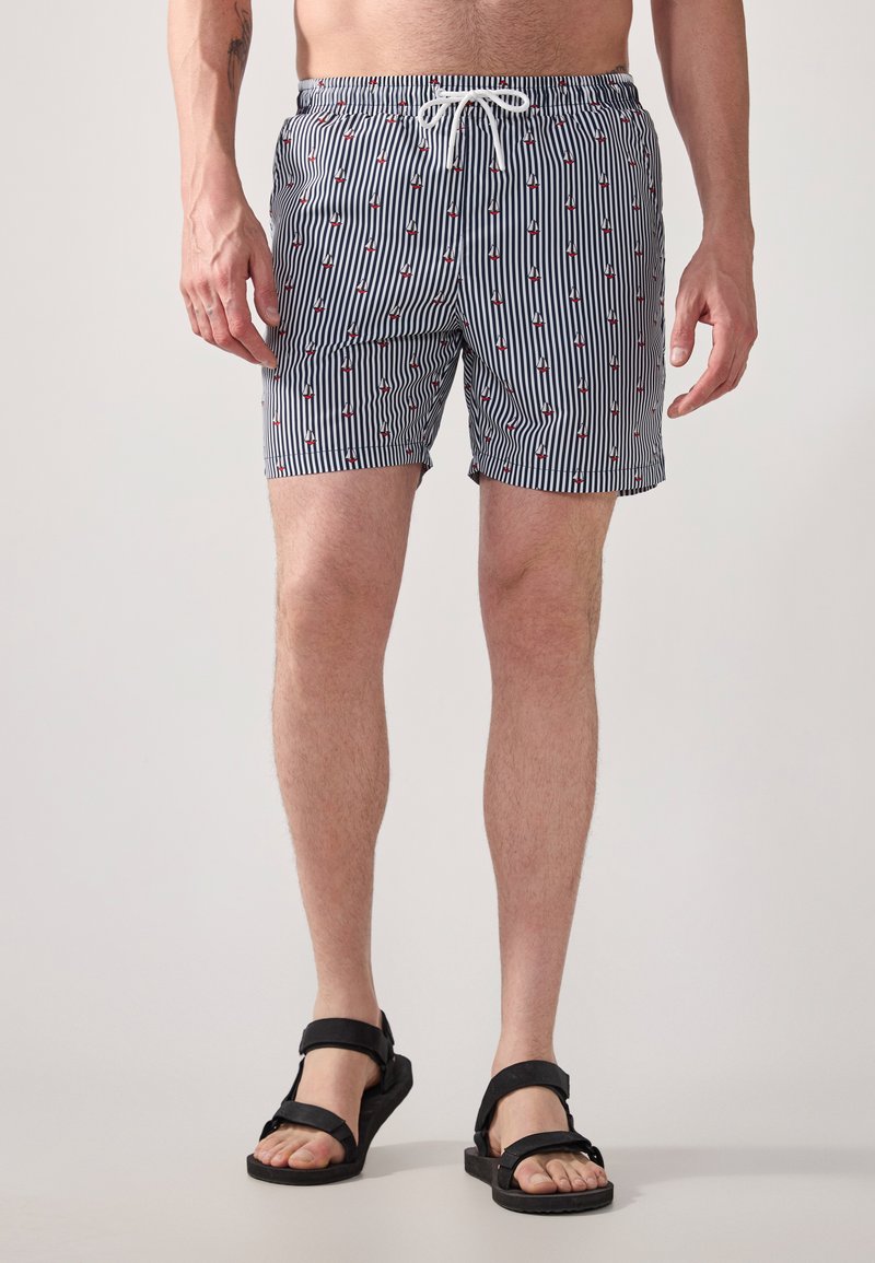 Gestreepte zwembroek in marineblauw en wit, met kleine rode ankerpatronen, voorzien van een elastische tailleband en trekkoord. Textuurstof.