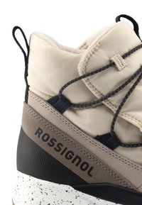 Bota alta beige con un exterior texturizado, acentos en negro, suela antideslizante y un destacado logo de "ROSSIGNOL" en el lateral.