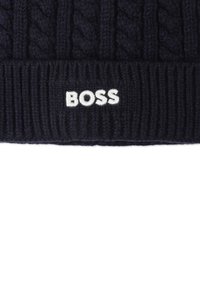 Bonnet en tricot bleu marine avec une texture côtelée et un motif en maille torsadée ; il présente un logo "BOSS" brodé en blanc à l'avant.