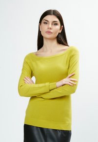 Maglione verde limone lavorato a maglia con scollo off-the-shoulder, polsini e orlo a coste. Texture morbida, design aderente e maniche lunghe.
