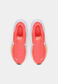 Φωτεινά κοραλλί και πορτοκαλί αθλητικά παπούτσια Nike με λευκές λογότυπο swoosh, δεμένα κορδόνια, φαίνονται από πάνω σε απλή φόντο.