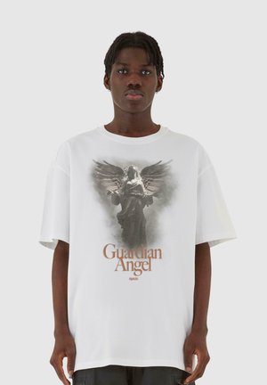 Hvit bomulls t-skjorte med grafisk trykk av en vinget engel og teksten "Guardian Angel" i brunt. Løs passform med korte ermer.