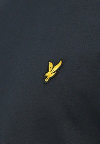 Temno modra bombažna majica z teksturirano tkanino, z rumenim izvezenim logotipom ptice na prsih, z okroglim izrezom in kratkimi rokavi.