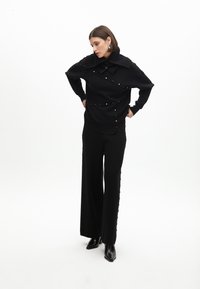 Černý pletený top s oversized límcem a zlatými knoflíky. Spárováno s černými širokými kalhotami s postranními knoflíky a střevíčky s špičatou špičkou.