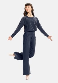 Dark grey long-sleeve top with a relaxed fit and high-waisted, wide-leg pants. Model wearing ballet shoes, striking a dance pose.