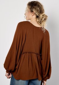 Top marrón de punto waffle con mangas largas y voluminosas y cintura peplum, que presenta un detalle con volantes en la línea de la cintura. Corte casual y tejido texturizado.