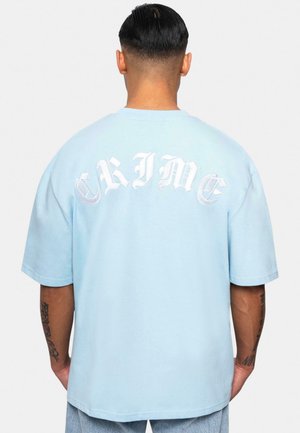 Svetlomodré oversized tričko vyrobené z bavlny, s výrazným bielym nápisom "CRIME" na chrbte a krátkymi rukávmi.