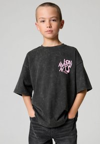 Sort oversized t-shirt med en falmet, tekstureret finish. Har et pink grafisk logo på venstre bryst. Bæres med mørke jeans.