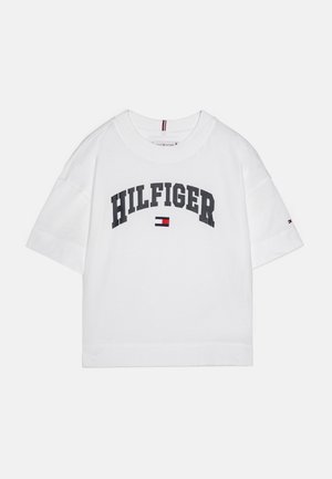 Biely bavlnený tričko s prehnanými krátkymi rukávmi, so značným čiernym logom "HILFIGER" a malým červeným, bielym a modrým emblémom.