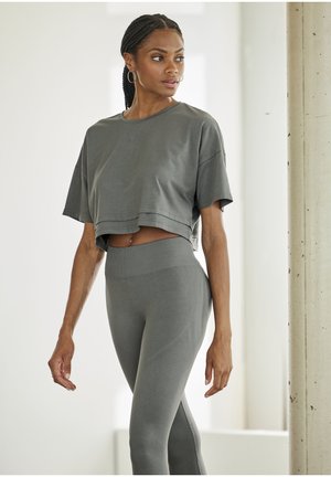 Graues, tailliertes T-Shirt mit kurzen Ärmeln und dezentem Logo, kombiniert mit hochgeschnittenen grauen Leggings, die strukturierte Akzente und ein nahtloses Design aufweisen.