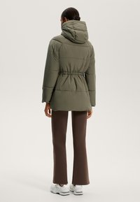 Olíva zöld, kapucnis steppelt dzseki, húzózsinórral a deréknál. Barna trapézfarmerrel és fehér tornacipővel párosítva.