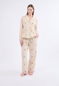 Pijama a rayas en beige claro con bordado floral. Presenta una camisa con botones y pantalones holgados con acentos rosas en los puños.