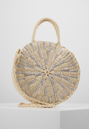 Pyöreä, punottu olkainen käsilaukku hopeanvärisillä metallisilla yksityiskohdilla, lyhyt kahva ylhäällä ja punottu olkahihna, esillä valkoisella pinnalla.