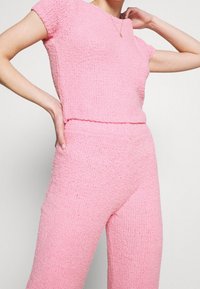 Różowy, teksturowany, dziany zestaw składający się z bluzki z krótkim rękawem i pasujących spodni, oba o miękkim, puszystym wyglądzie.