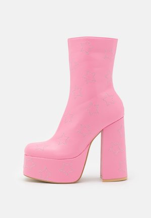 Botín de plataforma rosa con tacón alto de bloque y tachuelas plateadas en forma de estrella por toda la superficie.