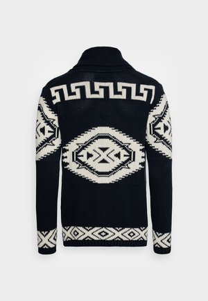 Strickpullover mit einem schwarz-weißen geometrischen Muster. Das Design umfasst auffällige Rauten und Zickzackmuster auf einer strukturierten Oberfläche.