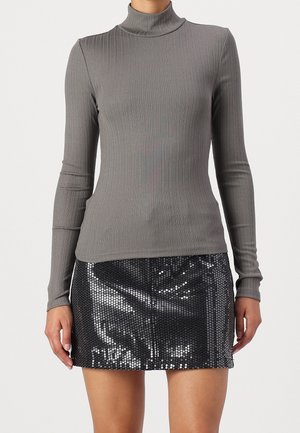 Kobieta ubrana w dopasowany, szary prążkowany golf z długim rękawem oraz czarną mini spódniczkę pokrytą lśniącymi cekinami.