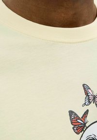 Lichtgele katoenen t-shirt met een ronde halslijn. Versierd met een grafiek van vlinders in zwart, roze en blauwe tinten. Soepele textuur.