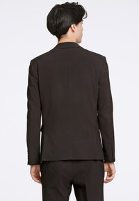 Zwarte colbert, slim-fit, gladde textuur, enkele split aan de achterkant en manchetten met knopen. Gestyled voor een moderne silhouet.