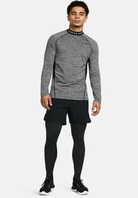 Maglietta a compressione grigia a maniche lunghe con dettagli neri; abbinata a pantaloni sportivi neri e leggings; presenta un collo rotondo e dettagli di texture.