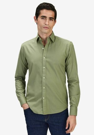 Grön långärmad skjorta med krage, tillverkad av mjukt tyg; har vita knappar och en regular fit-design. Bärs avslappnat med jeans.