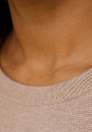 Gros plan sur le cou et la clavicule d'une personne portant un pull ras du cou en maille beige.