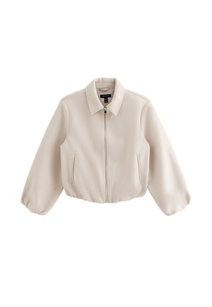 Veste beige à fermeture éclair avec manches longues bouffantes, col pointu et deux poches verticales à l'avant, présentée sur un fond blanc.