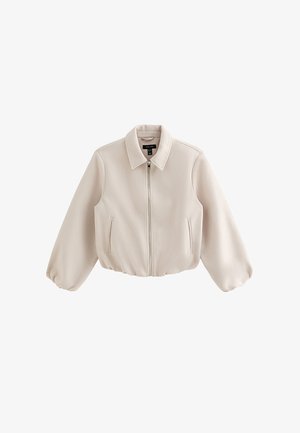 Veste beige à fermeture éclair avec manches longues bouffantes, col pointu et deux poches verticales à l'avant, présentée sur un fond blanc.