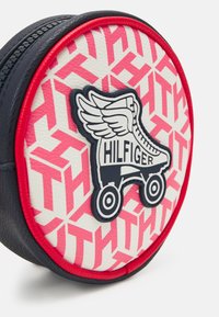 Custodia cosmetica rotonda realizzata in materiale testurizzato bianco e rosa a motivo, caratterizzata da una finitura blu navy e da un logo prominente di un pattino a rotelle con ali.