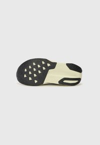 Semelle de chaussure en caoutchouc noir texturé, accents crème clair, motif de crampons triangulaire, et une découpe sur le côté pour flexibilité et adhérence.