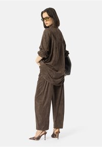 Conjunto de tela marrón y suave, con blusa holgada y pantalones de pierna ancha. Acentuado con tacones de estampado de leopardo. La modelo sostiene un bolso negro.