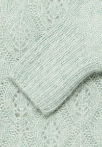 Tejido de punto verde claro con un patrón texturizado que presenta motivos de hojas y puños acanalados, destacando fibras suaves y peludas.