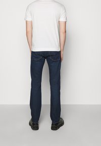 Blå denimjeans med rak passform, en lätt stretch och bakfickor med orange sömnad, tillsammans med en vanlig vit T-shirt.