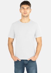 Weißes Baumwoll-T-Shirt mit kurzen Ärmeln, Rundhalsausschnitt und dezent gesticktem Logo auf der Brust, kombiniert mit blauen Jeans.