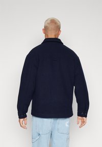 Marineblå uldjakke med krave, knappede ærmer og rygdetalje. Båret med lyseblå jeans, der har en afslappet pasform.