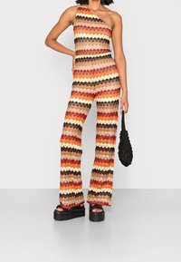 Enaxlad jumpsuit med ett zigzag-mönster i varma toner av röd, orange, gul och brun. Tillverkad av ett texturerat, lätt material.