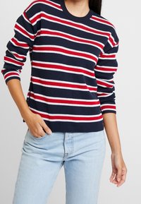 Pull côtelé bleu marine à rayures horizontales rouges et blanches. Col rond et manches longues. Tissu léger avec une coupe décontractée.