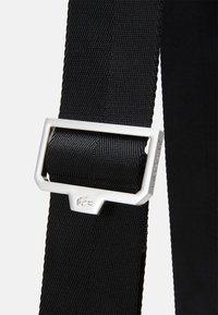 Black fabric belt with a textured surface and a silver metal buckle. The buckle features a logo and a rectangular design.