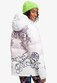 Puffervest i pink og hvid gradient med sorte blomster outlines. Hyggelig hætte og quiltet tekstur; parret med livlige mønstrede leggings.