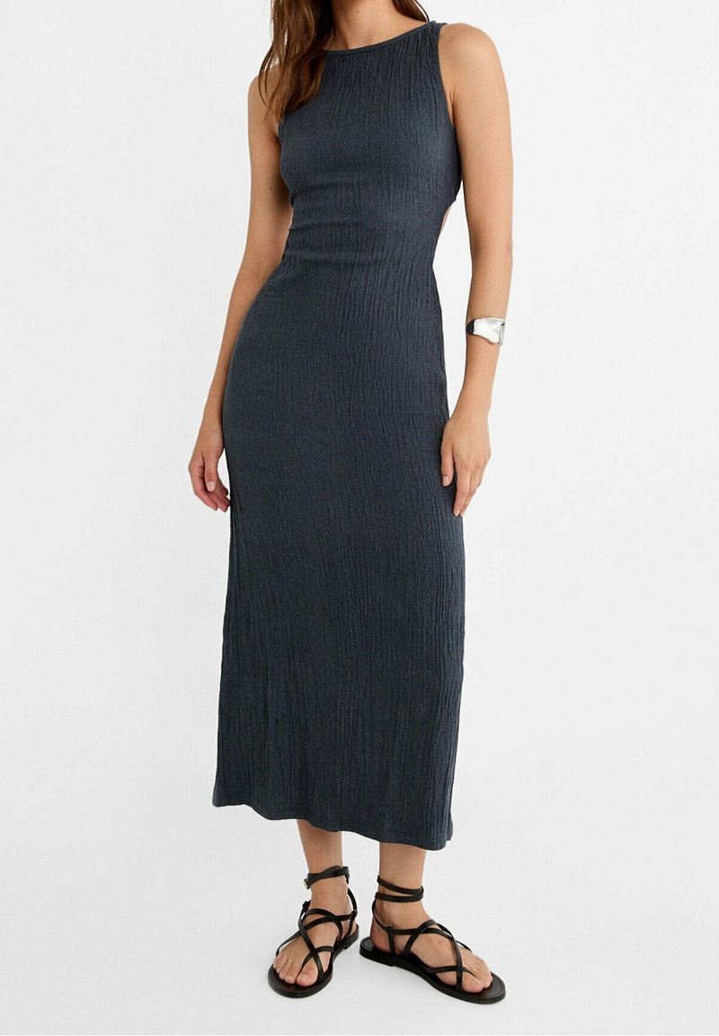 Robe midi sans manches gris foncé texturée avec une taille cintrée, portée avec des sandales plates noires à lacets et un large bracelet manchette argenté.