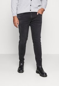 Černé slim fit džíny s mírně vybledlou strukturou, doplněné černými koženými kotníkovými botami. Outfit je doplněn šedým cardiganem.
