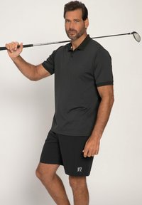 Polo skjorte i mørkegrå stof med krave og korte ærmer, parret med sorte shorts med et lille logo. En golfkølle hviler på skulderen.
