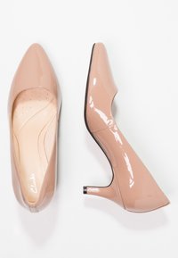 Talons hauts en cuir verni nude avec un design à bout pointu, accentués par un talon, et une texture lisse ; les semelles intérieures présentent de petites perforations pour plus de confort.
